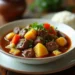 A bowl of hearty Hawaiian beef stew with tender beef, vegetables, and pineapple served with steamed rice on a rustic wooden table.